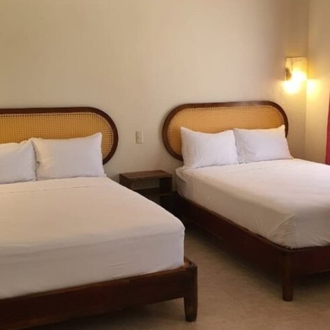 Zwei Einzelbetten mit weißen Bettlaken stehen in einem hellen Raum, beleuchtet von sanften Wandlampen.