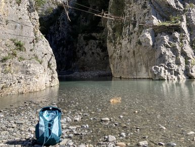 Ein schmaler Canyon mit steilen Felswänden, in dem ein ruhiger Fluss fließt und eine Hängebrücke sichtbar ist.