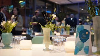 Ein eleganter Tisch mit Blumenarrangements und Kerzen, umgeben von Gästen in einem festlichen Raum.
