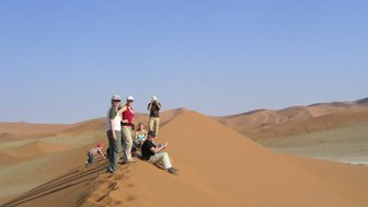 Eine Reisegruppe sitzt entspannt auf einer Sanddüne und genießt die Aussicht - Namibia Rundreise mit Kindern