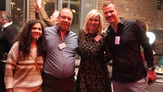 Eine Gruppe von vier Personen lächelt fröhlich in einem stilvollen Raum mit Backsteinwänden und gedämpftem Licht.