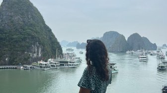 Eine Frau in einem blauen Kleid steht an einem Geländer und blickt auf die beeindruckende Halong-Bucht mit ihren Felsen.