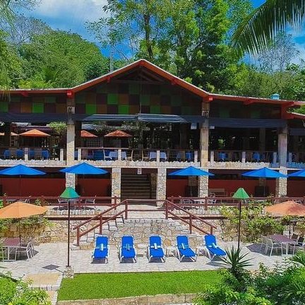 Ein farbenfrohes Resort mit einer großen Terrasse, umgeben von üppigem Grün und Sonnenschirmen in verschiedenen Farben.