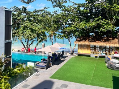 Ein luxuriöser Poolbereich mit Liegen und Sonnenschirmen, umgeben von Palmen und Blick auf das glitzernde Wasser.