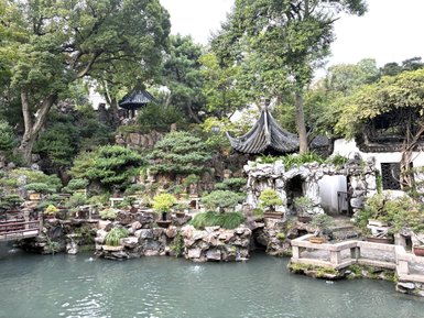 Ein malerischer Garten in Shanghai mit üppigem Grün, Steinen und einem ruhigen Wasserlauf, der eine friedliche Atmosphäre schafft.