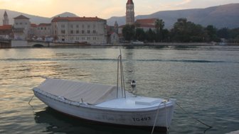 Ein kleines Boot mit einer weißen Plane schaukelt sanft im Wasser, während die Stadt im Hintergrund in der Dämmerung leuchtet.