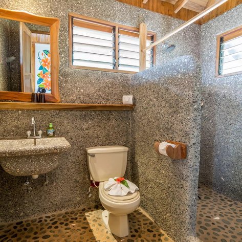 Ein modernes Badezimmer mit steinähnlichen Wänden, einem eleganten Waschbecken und einem Holztuchhalter, das einen tropischen Flair vermittelt.