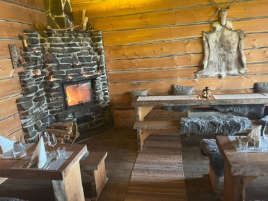 Ein gemütliches Restaurant mit Holzwänden, einem Steinofen und rustikalen Holzmöbeln, die eine warme Atmosphäre schaffen.