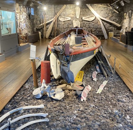 Ein historisches Boot steht in einem Museum, umgeben von Steinen und verschiedenen maritimen Artefakten an den Wänden.