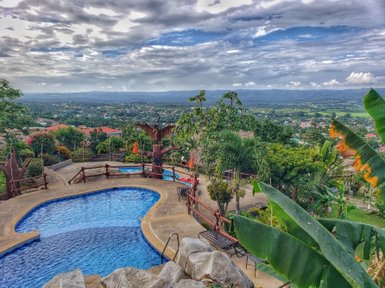 Ein atemberaubender Blick auf einen Pool, umgeben von üppigem Grün und einer malerischen Landschaft unter einem bewölkten Himmel.