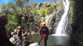 Eine Gruppe von Canyoning-Anfängern steht an einem Wasserfall, bereit, das Abenteuer im klaren Wasser zu beginnen.
