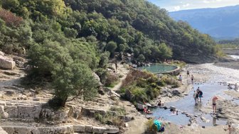 Eine Gruppe von Menschen genießt das Wasser in einem natürlichen Pool, umgeben von üppigem Grün und sanften Hügeln.