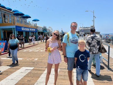 Eine Familie steht auf der Santa Monica Promenade, umgeben von Menschen und bunten Geschäften unter strahlendem Sonnenschein.
