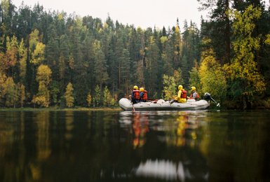 Eine Gruppe von fünf Personen in einem Schlauchboot auf einem ruhigen Fluss, umgeben von buntem Herbstlaub.