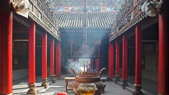 Ein traditioneller chinesischer Tempel mit roten Säulen, einem großen Räuchergefäß und aufsteigendem Rauch im Innenhof.