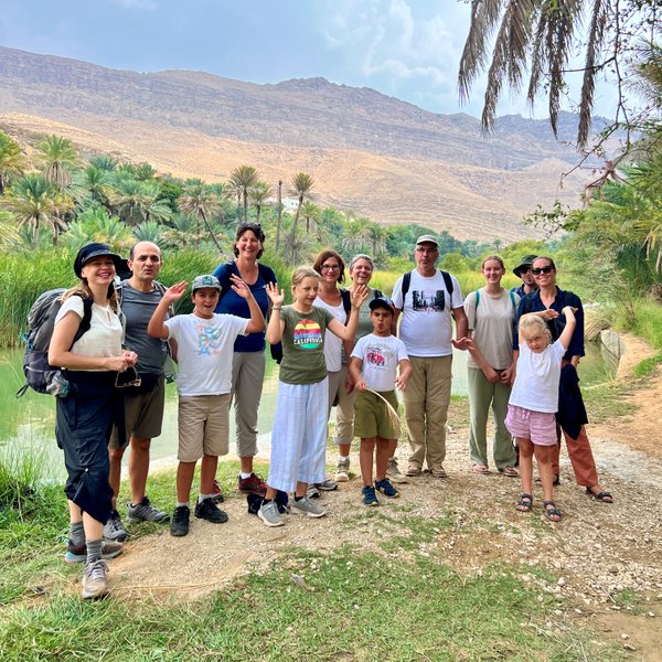 Gruppe posiert für Foto im Wadi Shab mit Bergen im Hintergrund – Oman Familienreise