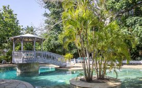 Ein malerischer Pool mit einer Holzbrücke und üppigem Grün umgibt die entspannende Atmosphäre des Resorts.
