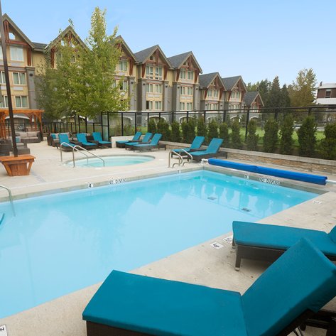 Ein einladender Poolbereich mit Liegen und einem Whirlpool, umgeben von Bäumen und einem modernen Gebäude im Hintergrund.