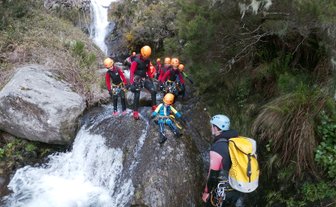 Eine Gruppe von Canyoning-Abenteurern steht an einem Wasserfall, bereit, den nächsten Abschnitt des Flusses zu erkunden.