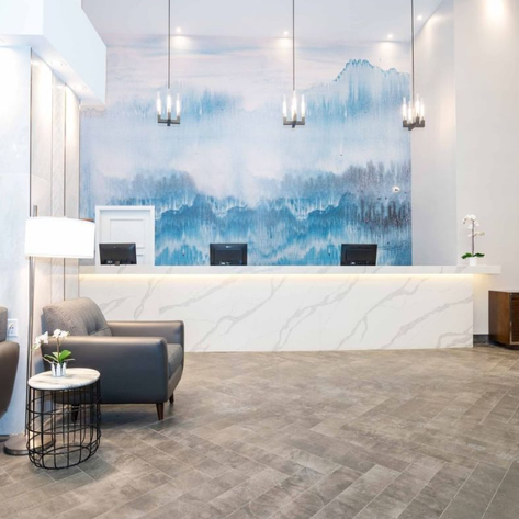 Der Empfangsbereich eines modernen Hotels mit eleganter Beleuchtung und einem beruhigenden Wandgemälde in Blau- und Grautönen.