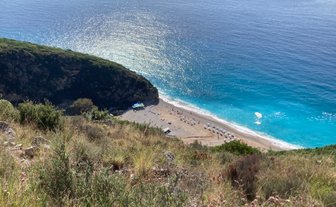 Ein atemberaubender Blick auf den Gjipe Strand, umgeben von grünen Hügeln und glitzerndem, blauem Wasser.