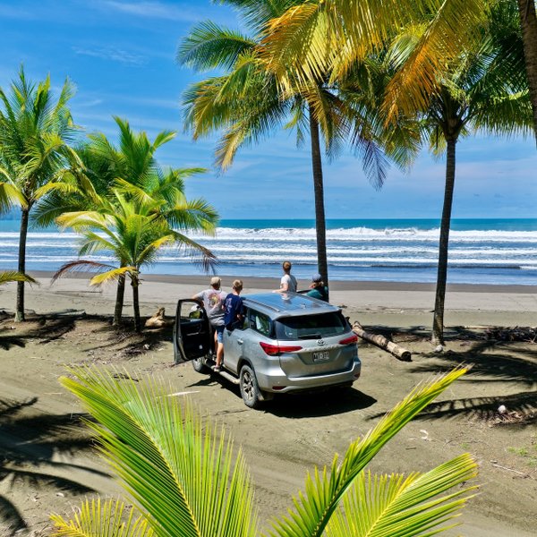 Am Strand von Playa Quepos stehen vier Personen, die das Ocean-View bewundern, während ein Auto im Sand parkt.