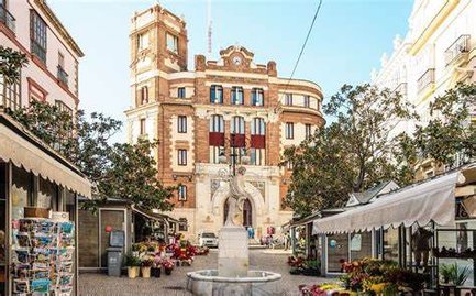 Ein belebter Platz in Cádiz mit einem historischen Gebäude im Hintergrund und bunten Blumenständen im Vordergrund.