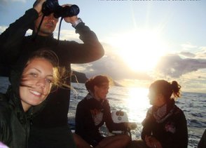 Eine Gruppe von vier Personen auf einem Boot, während die Sonne über dem Wasser untergeht, erzeugt eine entspannte Atmosphäre.