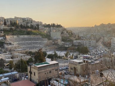 Das römische Theater in Amman ist von modernen Gebäuden umgeben, während die Sonne hinter den Hügeln untergeht.