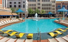 Ein einladender Pool mit klarem Wasser, umgeben von gelben Liegen und schattenspendenden Sonnenschirmen in einer urbanen Umgebung.