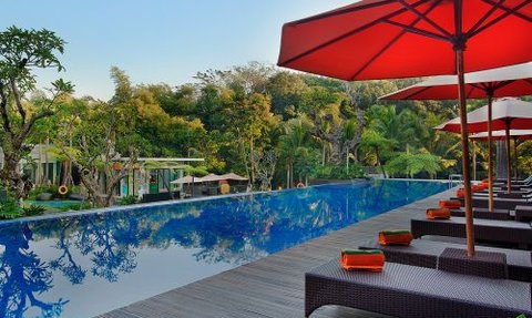 Ein luxuriöser Pool mit reflektierendem Wasser, umgeben von üppigem Grün und Sonnenschirmen in einem tropischen Resort.