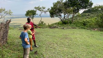 Ein Maasai zeigt zwei Kinder die Umgebung während eines Naturspaziergangs in der afrikanischen Landschaft.