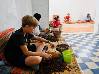 Kind hilft einheimischen Frauen beim Mahlen von Arganfrüchten zur Ölgewinnung in Essaouira – Marokko Familienreise