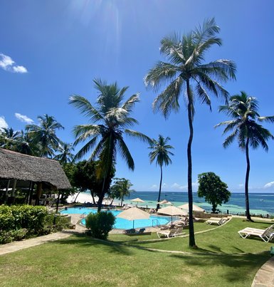 Ein tropisches Resort mit Palmen, einem Pool und Blick auf den Ozean unter einem strahlend blauen Himmel.