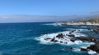 Ein atemberaubender Blick auf das tiefblaue Meer, das sanft gegen die schwarzen Felsen brandet, unter einem strahlend blauen Himmel.