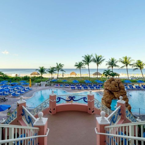 Ein Blick auf den Poolbereich des Resorts, umgeben von blauen Liegen und Palmen, mit dem Meer im Hintergrund.