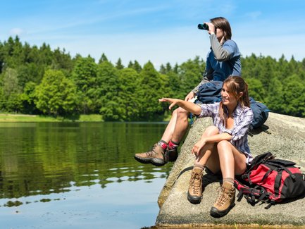 Zwei Jugendliche sitzen auf einem Felsen am Wasser, während einer mit einem Fernglas in die Ferne schaut.