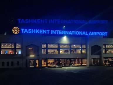 Das beleuchtete Gebäude des internationalen Flughafens Taschkent strahlt in der Dunkelheit mit blauen Lichtern und reflektiert den Namen.
