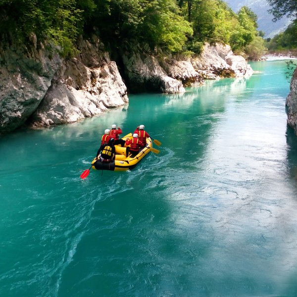 Eine Gruppe von vier Personen paddelt in einem gelben Schlauchboot auf einem klaren, türkisfarbenen Fluss, umgeben von Felsen.