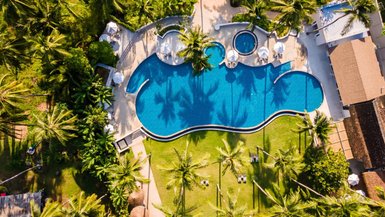 Ein luftiger Blick auf einen großen Pool, umgeben von Palmen und Liegen, ideal für Entspannung und Erholung.