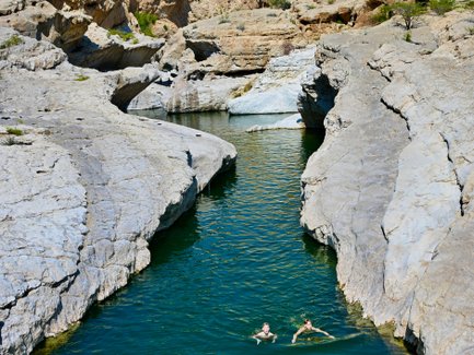 Kinder schwimmen im Wasser zwischen Felsen im Wadi Bani Khalid im Oman – Oman Familienreise