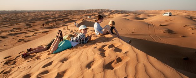 Kinder sitzen gemeinsam auf einer Wüstendüne – Oman Familienreise