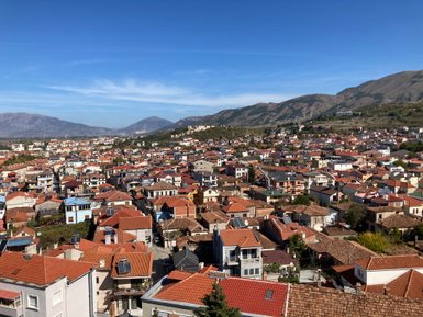 Eine weite Aussicht auf die Stadt Korça, mit zahlreichen Häusern und roten Dächern, umgeben von sanften Hügeln.