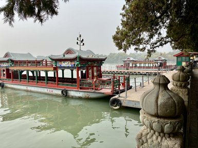 Ein traditionelles chinesisches Boot liegt am Ufer eines ruhigen Gewässers, umgeben von malerischen Pavillons und Bäumen.