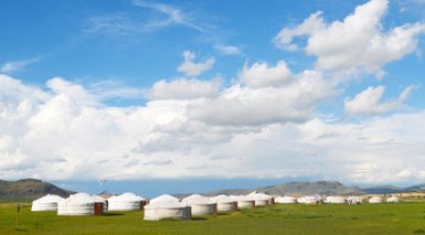 Eine weite Landschaft mit mehreren Jurten, umgeben von saftigem Grün und unter einem strahlend blauen Himmel.