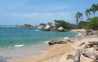 Ein ruhiger Strand mit sanften Wellen, umgeben von großen Felsen und üppigen Palmen im Hintergrund.