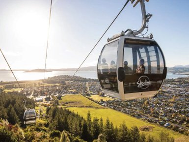 Eine Gondel schwebt über die malerische Landschaft von Rotorua, mit Blick auf den glitzernden See und die Stadt darunter.