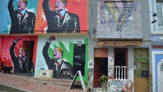 Bunte Graffiti an einer Wand zeigen einen leidenschaftlichen Redner mit erhobener Faust, umgeben von lebhaften Farben.