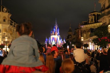Eine Menschenmenge bewundert das beleuchtete Schloss im Magic Kingdom, während Kinder auf den Schultern ihrer Eltern sitzen.
