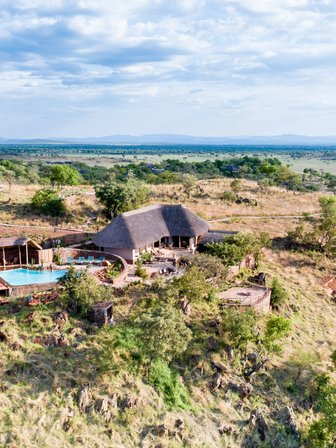 Eine atemberaubende Aussicht auf die Ikoma Hills Lodge, umgeben von sanften Hügeln und üppiger Vegetation in Tansania.